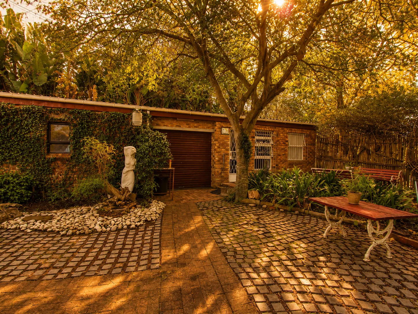 Golden late afternoon courtyard at Protea Guesthouse in Durbanville with garden seating and mature trees